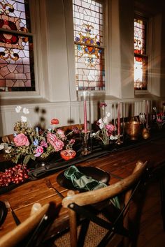 a wooden table topped with lots of flowers next to two stained glass windows in a church