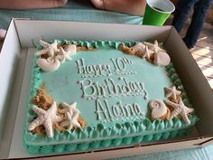 a birthday cake in a box with starfish and shells on the top, sitting on a table