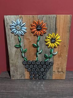 an art piece made out of recycled wood and decorated with flowers on the side, sitting on a table