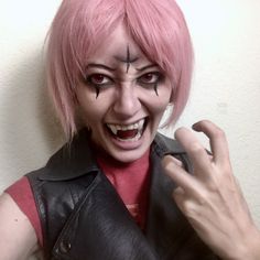 a woman with pink hair and makeup holding her hand up to the camera while wearing a black leather vest