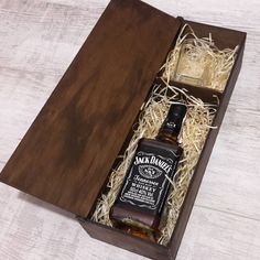 an open wooden box containing two bottles of jack daniels whiskey and some straw on the floor