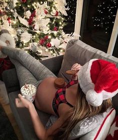 a woman laying on a couch with her legs crossed and eating popcorn in front of a christmas tree