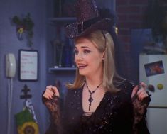 a woman wearing a witches hat in the kitchen with her hand on her hip and pointing at something