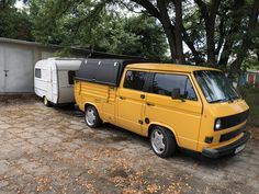 a yellow van parked next to a white trailer on a brick road with trees in the background