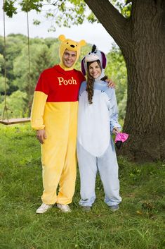 man and woman in winnie the pooh costume standing next to each other under a tree