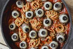 a pan filled with pasta covered in googly eyes and black olives on top