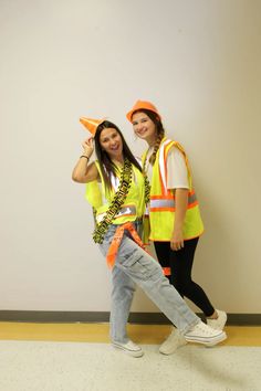 two women in safety vests posing for a photo together with orange cones on their heads