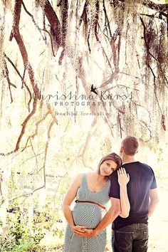 a pregnant couple standing under a large tree