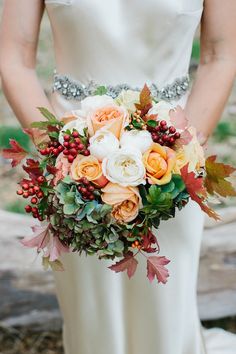 a woman holding a bouquet of flowers in her hands and wearing a white dress with an orange, yellow, and red color scheme