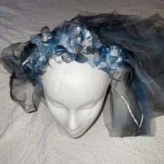 a white mannequin headpiece with blue flowers on it's side and tulle