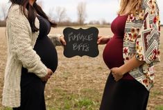 two pregnant women standing in a field holding a chalkboard