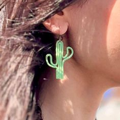 a woman wearing green earrings with a cactus design