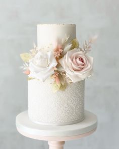 a white wedding cake with pink flowers and leaves on the top tier, sitting on a pedestal