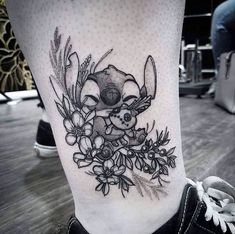 a black and white tattoo on the leg of a person with flowers in front of them