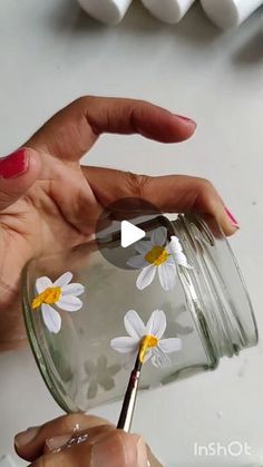 a woman is painting daisies in a jar