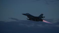 a fighter jet flying through the sky at night with red light coming from it's tail