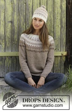 a woman sitting on the ground wearing a sweater and hat