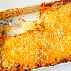 a casserole dish is covered with cheese and has a spatula in it