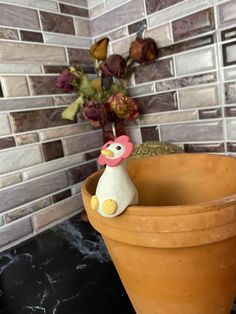 a clay pot with a chicken sitting in it next to a vase filled with flowers