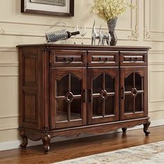 a wooden sideboard with two wine glasses on top and flowers in vases next to it