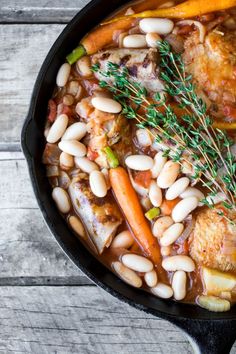 a skillet filled with meat, beans and carrots on top of a wooden table