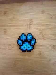 a piece of art made out of perler beads on a wooden surface with a black and blue cat's paw