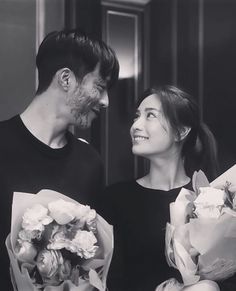 the man and woman are holding bouquets of flowers in front of each other, smiling