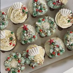 twelve cupcakes decorated with white frosting and christmas decorations on a baking sheet