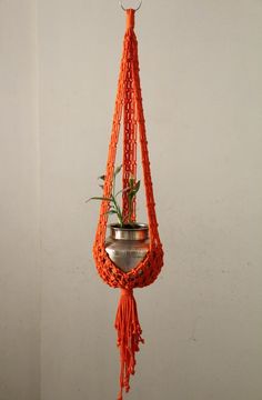 an orange macrament hanging from a hook with a potted plant in it