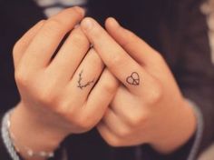 a woman holding her hands together with two hearts tattooed on their fingers and the other hand