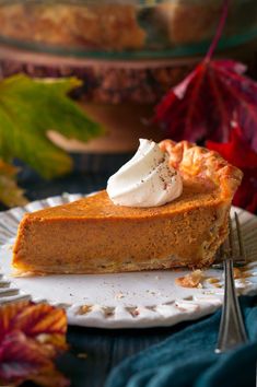 a slice of pumpkin pie on a plate with a fork and fall leaves in the background