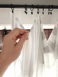 a hand is holding the curtain rod to open it in front of two white striped curtains