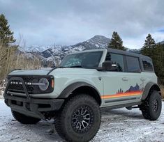 a white truck parked on top of a snow covered ground next to trees and mountains