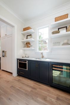 a kitchen with white walls and wooden floors, open shelving above the sink area