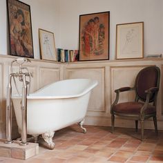 an old fashioned bathtub in a bathroom with pictures on the wall and chair next to it