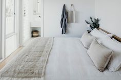 a bed with white linens and pillows in a bedroom next to a door that leads to another room