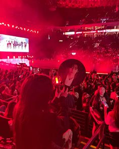 a large crowd at a concert with red lights and people in the stands holding up cell phones