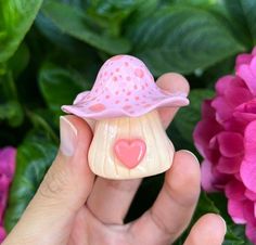 a hand holding a small toy with a hat on it's head and pink flowers in the background