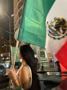 a woman holding an american and mexican flag in front of a city street at night