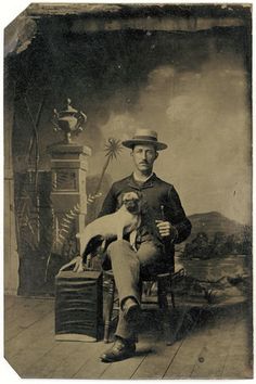 an old black and white photo of a man sitting in a chair holding a dog