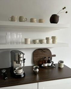 there are many cups and saucers on the shelf above the coffee maker in this kitchen