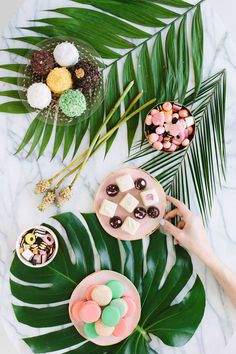 a table topped with plates and bowls filled with desserts next to palm leaf leaves