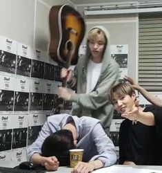 three people sitting at a table in front of a wall with guitars hanging on it