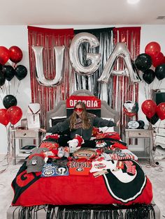 a woman sitting on top of a bed surrounded by red and black balloons in the shape of letters