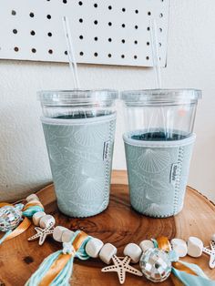 two cups with straws on top of a wooden table next to beads and seashells