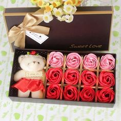 a teddy bear sitting next to some cupcakes in a box with flowers on the table