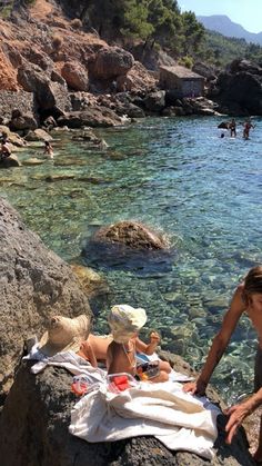 two people are sitting on rocks near the water and one person is holding a towel