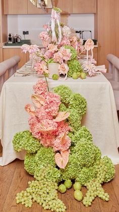 the table is covered with flowers and green grapes in front of an arrangement of pink carnations