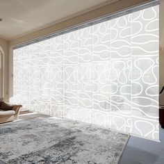 a living room with an area rug and large window covered in white decorative glass panels