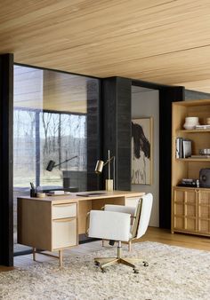 an office area with a desk, chair and bookshelf in front of large windows